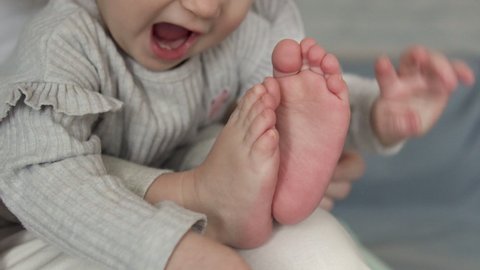 Cute curious pretty little baby playing with legs, counting toes, tickling feet