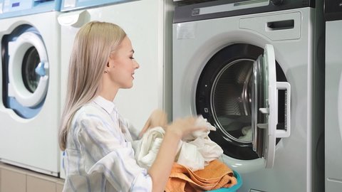 Washing machine washes dirty laundry, woman takes clean laundry out of washing machine, public self-service laundry. slow-motion