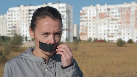 Freedom of speech concept. The woman removes the tape from her mouth.