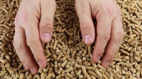 hands picking up wood pellets and pouring them on a pile