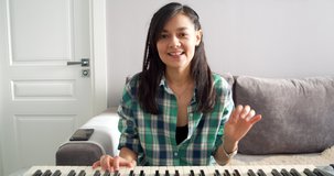 Young woman music teacher playing electric piano talking to web camera teaching remotely online using laptop while working from home. Telework concept. Webcam view.