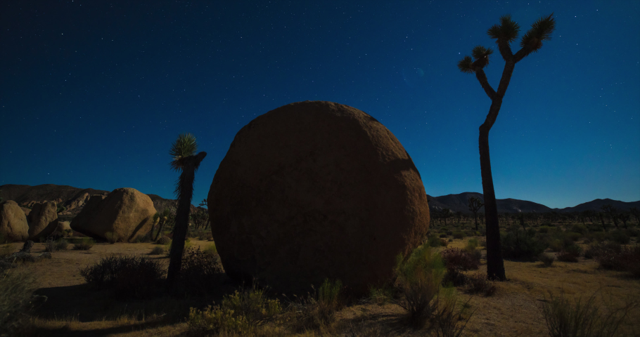 Sphere shaped jumbo rock in Joshua Tree National Park under a starry, moonlit sky of deepest blue.