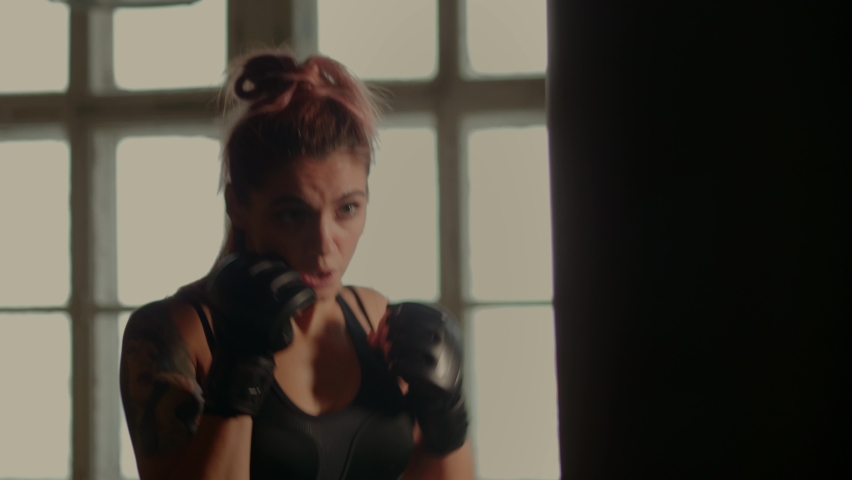 4k video of athletic female fighter exercising with punching bag in gym during kickboxing and self defense workout | Shutterstock HD Video #1067634671