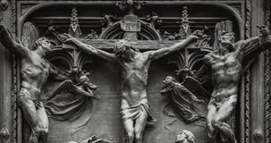 Statues of crusified Jesus and two criminal bandits filmed in close up on main entrance gate of Duomo di Milano,main christian catholic church in Italy
