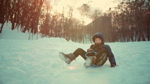 slow motion of funny kid boy sliding on snow saucer sled outdoors in winter