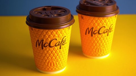 Ukraine, Kyiv - February 17, 2021: Yellow glass of coffee from McDonald's. Paper glass drink Mc Cafe. Two coffee cups on table with shadows. Menu in fastfood restaurant. Blue background.