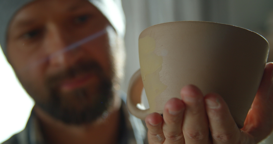Male potter painting a cup in his hands with a brush. Men making ceramic item. Pottery working, handmade and creative skills.