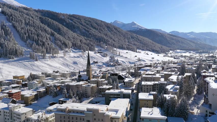Davos, Switzerland. Aerial view of famous Swiss Alpine ski resort town in winter, buildings and slopes covered in snow, clear blue sky - landscape panorama of Alps mountain range from above, Europe.
