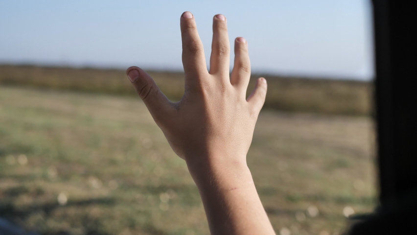 A teenager boy traveling by car waving his hand at the open window of a car breathing fresh air of the countryside, his hand moving in the wind | Shutterstock HD Video #1067645672