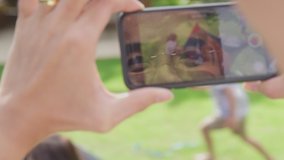 Close up of Asian father recording video on mobile phone as mother and children put up tent in garden at home - shot in slow motion
