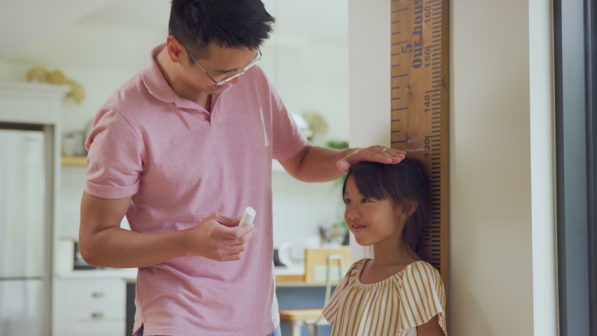 Excited Asian girl being measured by father at home against oversized ruler - shot in slow motion | Shutterstock HD Video #1067645726