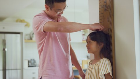 Excited Asian girl being measured by father at home against oversized ruler - shot in slow motion