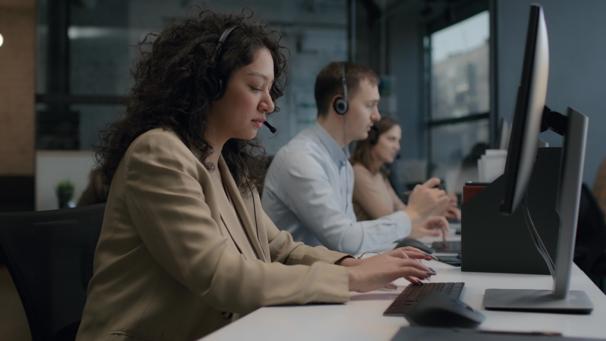 Call center and helpful customer service. Use desktop pc at computer table and phone line at modern co-working. Diverse group of workers talks on sale hotline. Busy seller at agency office close-up Royalty-Free Stock Footage #1067649053