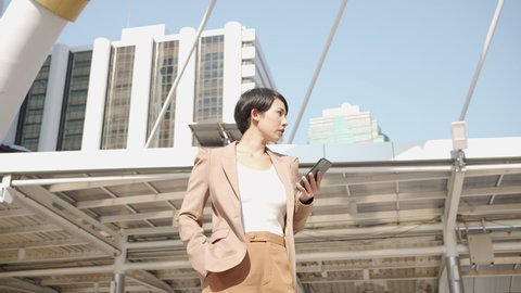 360 Degree shot of  Asian young businesswoman holding smartphone looking new job in the city, Standing in middle of building in capital. Camera moving around freelance woman, businesswoman slow motion