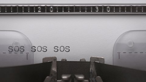 Typing text SOS on vintage manual typewriter. Close up of writes word on white paper. Shot in macro 4K resolution. Typing a Morse code distress signal - The phrase save our souls.