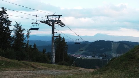Ski lift moving with hardly any tourists during lockdown. Empty seats in cable cars. View from the top of the hill. Beautiful scenic summer landscape, evening in the blue mountains, forest around.