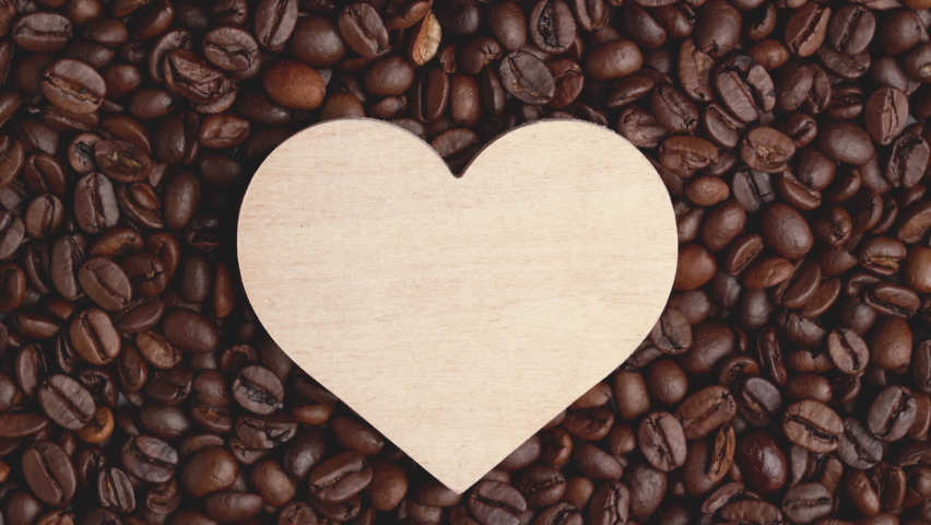 Wooden heart symbol rotates lying on roasted coffee beans