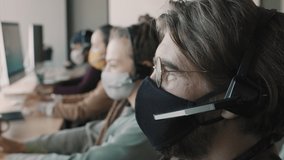 Close up shot of young man in face mask and headset working in call center and answering inquiries - Powered by Shutterstock - Get 15% off with code: PIKWIZARD15