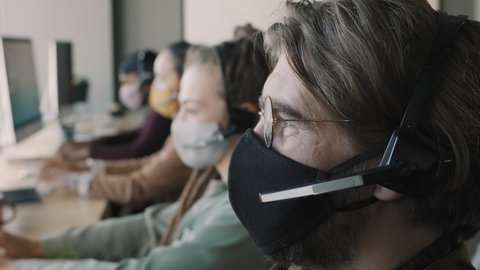 Close up shot of young man in face mask and headset working in call center and answering inquiries Stockvideó