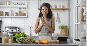 POV of a young, happy and beautiful Asian woman with curly long hair wearing grey gingham apron. She's makes video about making meal or live streaming online to show cooking method in modern kitchen.
