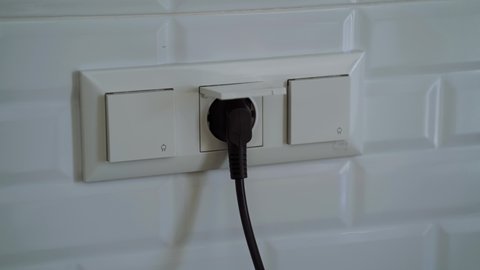 Close-up of a woman's hand unplugging and plugging power cable into the socket. Inserting and removal electrical power cord plug. Receptacle and wall outlet.