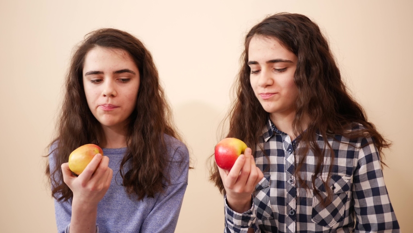 Teenager sisters cute twin girls together have fun eating ripe apples - two kids portrait bite and chew fruits
