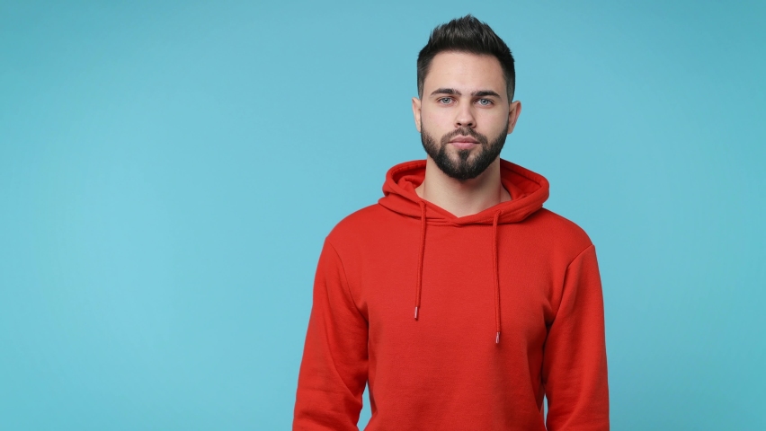 Displeased bearded young man 20s wearing casual red streetwear hoodie isolated on pastel blue color background in studio. People lifestyle concept. Say no holding folded crossed hands in stop gesture Royalty-Free Stock Footage #1067663369