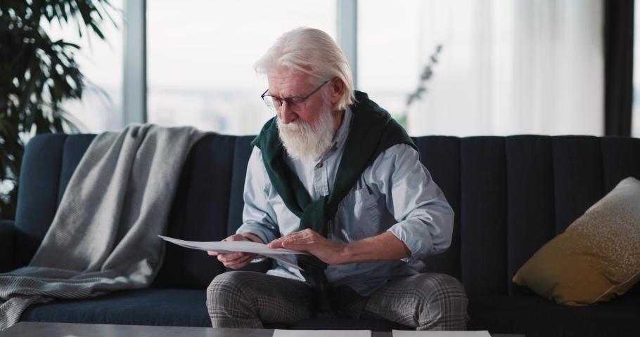 Mature handsome grey haired bearded man working with office papers counting bills sitting at home during quarantine. Businessman. Lifestyle. | Shutterstock HD Video #1067663501