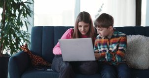 Couple of caucasian cute children using laptop computer connecting internet social media typing messages and watching fun video content together.