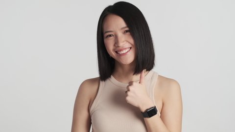 Beautiful Asian girl looking happy showing okay and thumb up gesture on camera over white background. Like it gesture