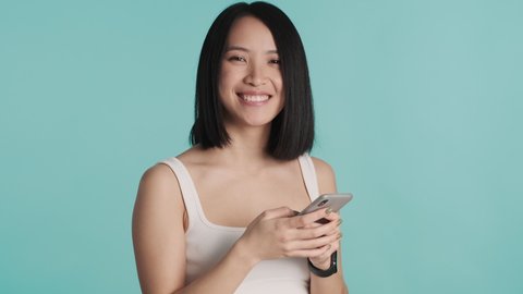 Attractive Asian girl browsing social network and smiling on camera over colorful background. Modern technology