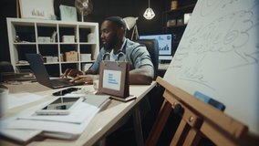 Smiling african american guy using computer in hipster office. Positive afro businessman talking online in late night coworking. Handsome african man having video call at workplace.