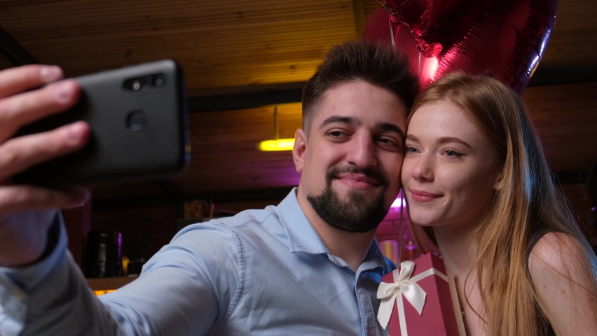 Lovely couple making a selfie while holding valentines gift and air balloons