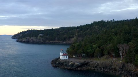 Lighthouse drone. Drone flying around lighthouse at sunset in the Pacific North West San Juan Islands. Birds flying over ocean with forest in background. Lighthouse