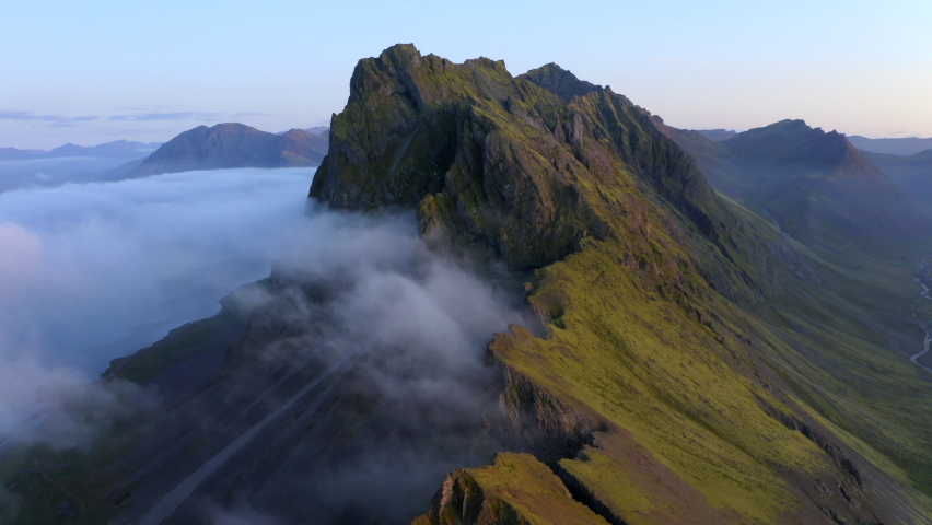Drone aerial footage of Coastal mountains and cliffs near Stokkness at sunrise with clouds in Iceland