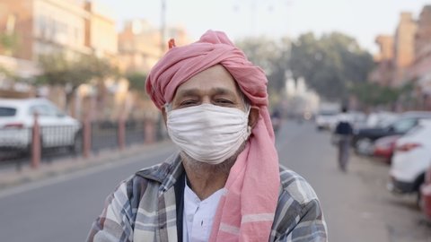 A smiling local traditional Indian Asian farmer wearing turban standing in the city removes the protective face mask looking at the camera amid COVID 19 epidemic. Post-vaccination concept 