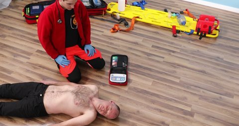 Reanimation of patient with defibrillator. Male paramedic in red scrubs teaching students correct procedure on using defibrillator machine. Application