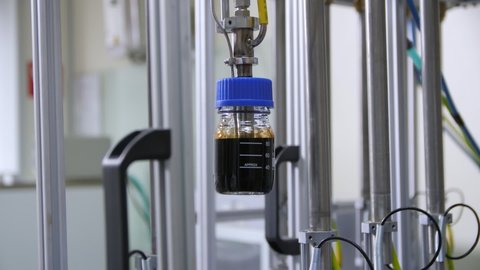 Woman controls putting bottle of crude oil into special automatic testing equipment in modern laboratory close view