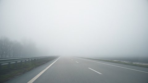 Driver POV of empty grey foggy misty rainy highway intercity road with low poor visibility on cold spring ar autumn morning. Seasonal bad rainy weather accident danger warning