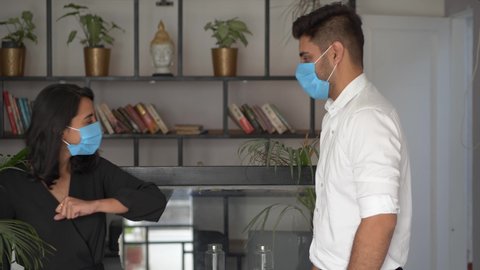 Indian business man and woman wearing medical face masks greeting with elbow bump and talking during office break.Two colleagues avoid touch for coronavirus protection talking and chatting cheerfully.