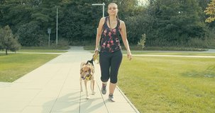 Woman of runner and dog on city street under sunrise sky in morning time. Outdoor walking. Athletic young girl with his dog are running in town. 4K video