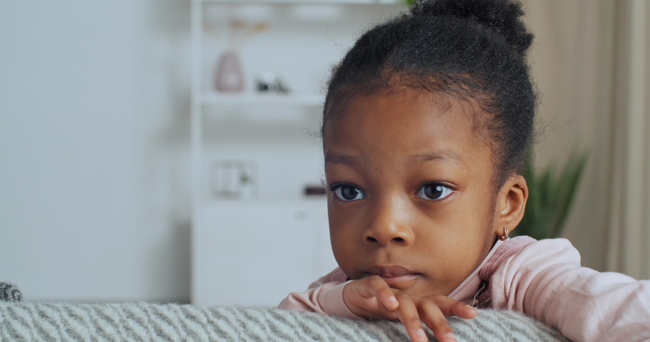 Portrait of afro american child little girl with dark skin and large wide open eyes looks at camera emotions of sadness stress, close-up of calm face of toddler indoors, orphan kid missing his family Royalty-Free Stock Footage #1067692508