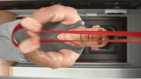Muscular Athletic Man Exercising Fitness Rubber Bands at Home in Hallway. Fitness Classes Without Leaving Home. Mindful Living, New Beginning, Self-improvement, Personal Growth Workout. Vertical Video
