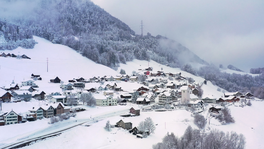 Walensee, Switzerland: Aerial view of village Obstalden near Lake Walen (Lake Walenstadt) in winter, landscape and trees covered in snow - panorama of Swiss Alps mountain range from above, Europe