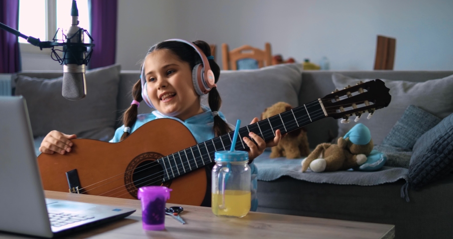 Little girl plays guitar and sings in her video blog, live stream recording, fun for kids, virtual socializing, recording tutorials Royalty-Free Stock Footage #1067696996