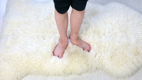 Close up of young girl child standing with bare feet toes on very soft woolen sheepskin rug carpet. Cozy winter concept. Top view.