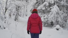 Girl in bright winter clothes walks through the snowy forest