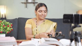 Indian woman preparing for online class by wearing headphone and looking into books in front of mobile phone at home - Concept of virtual education and new normal lifestyle.