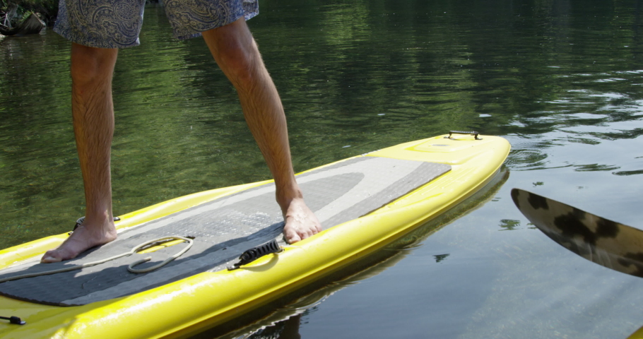 Paddle boarder coming in to shore - close up on paddle board and legs