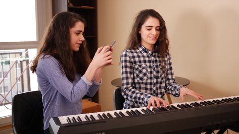 Teenage girl shoot phone social media stories of her twin sister playing electro piano music melody